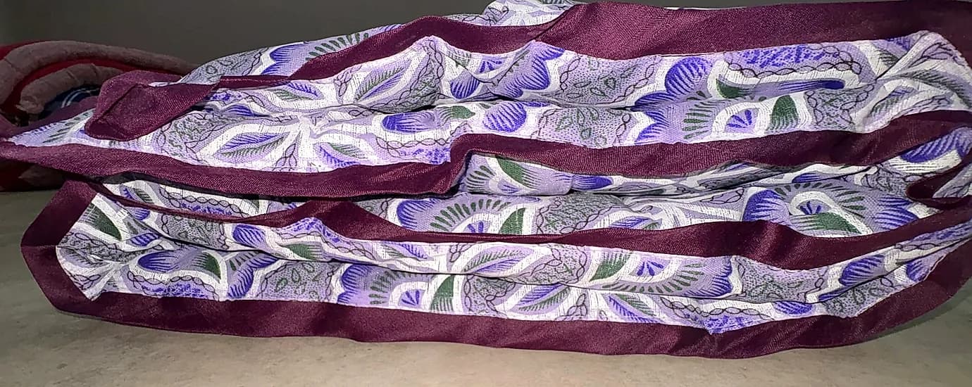 Folded stack of purple and white floral vine quilts with satin piped edges
